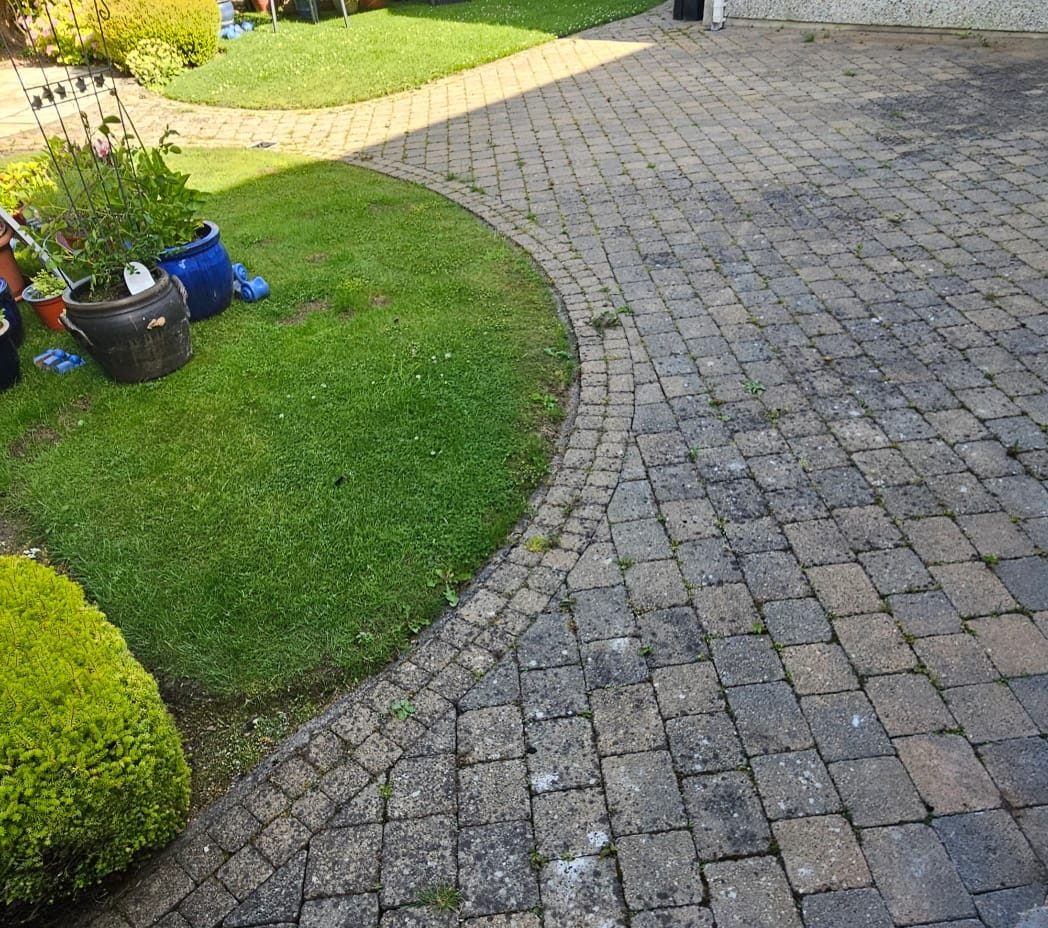 Curved block paving driveway before cleaning — grime and weeds dulling the surface