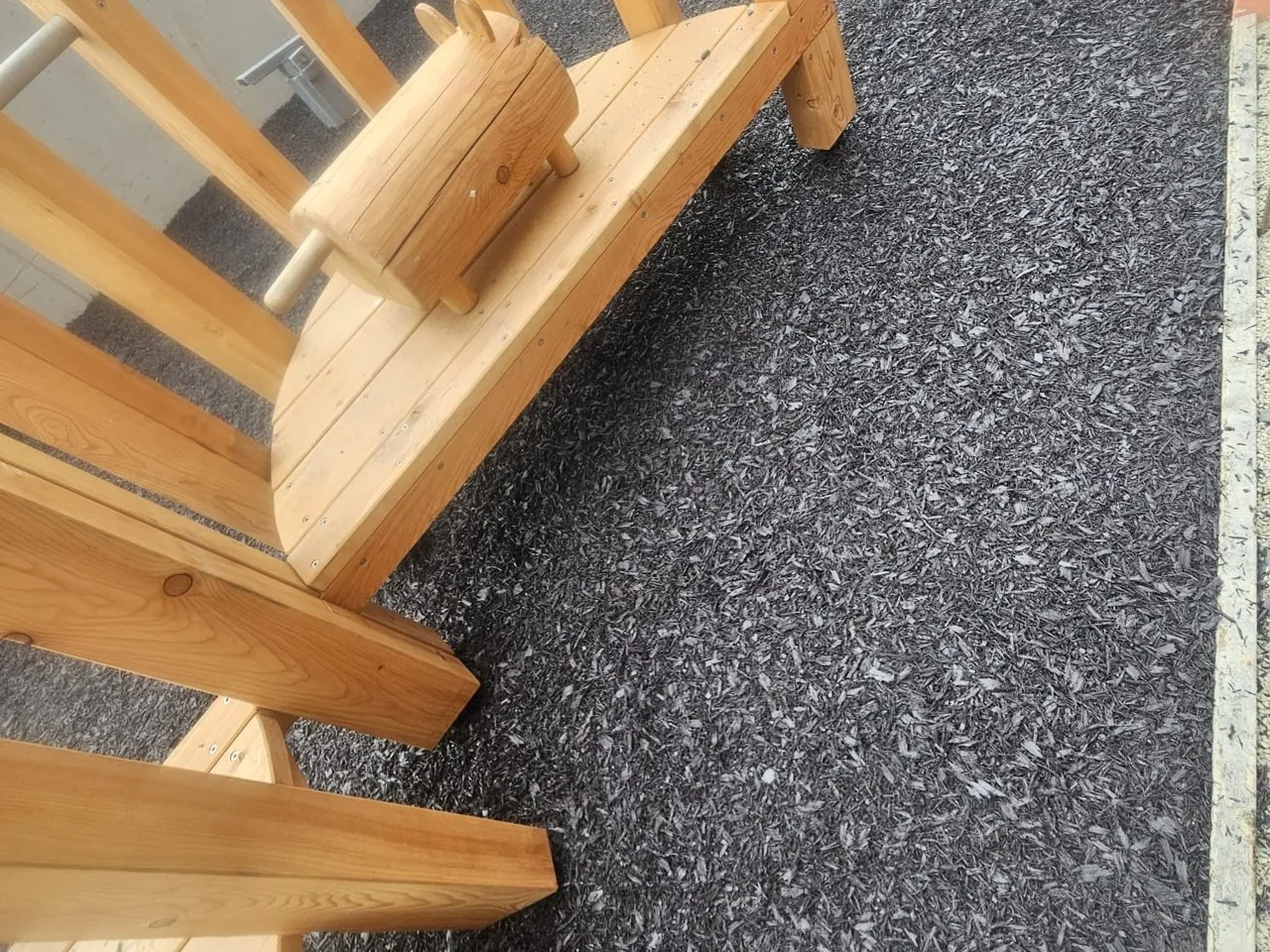 Close-up of resin bound rubber mulch finished flush around the feet of timber play equipment, Tallaght